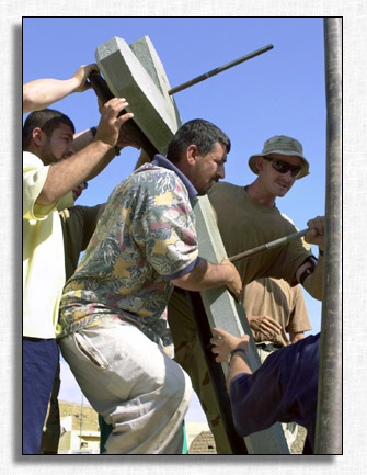 Iraqi men lift concrete Cross.